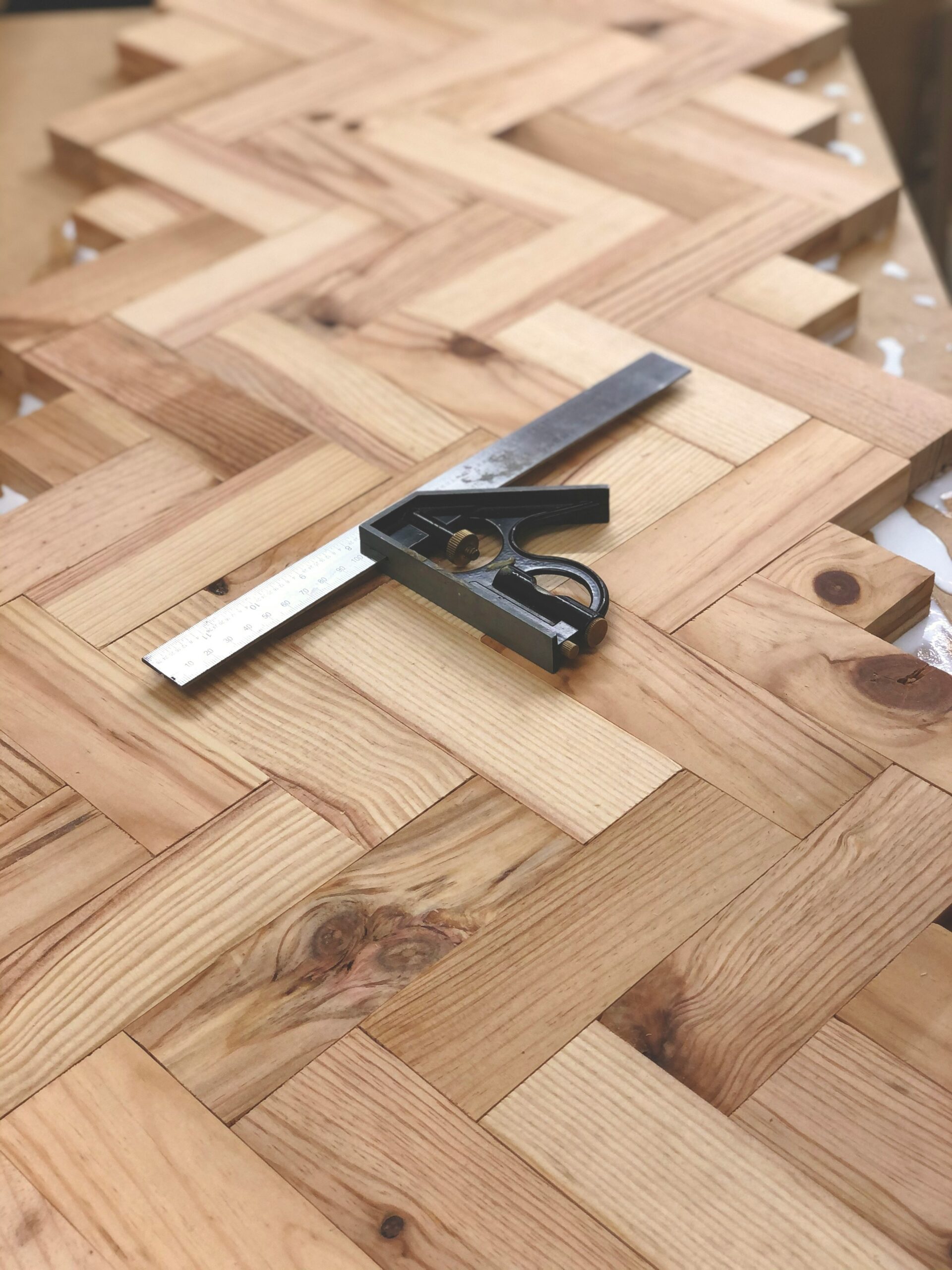 Herringbone wood floor being laid, checked with a combination square, which only stays tight and true on a flat subfloor