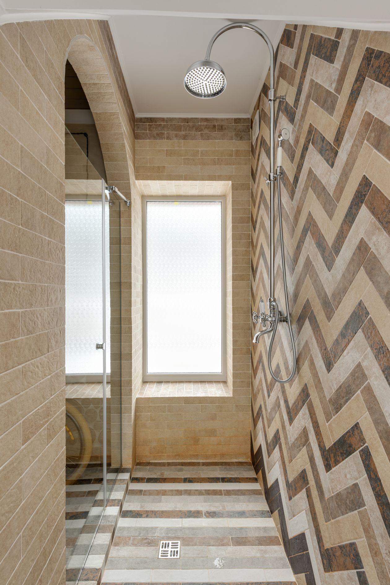 Close-up of long, narrow herringbone tiles on a walk-in shower wall, showing the stepped zig-zag pattern