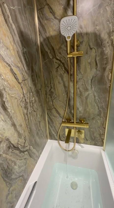 Brushed gold bathroom with gold thermostatic shower over bath and marble-effect walls in Liverpool