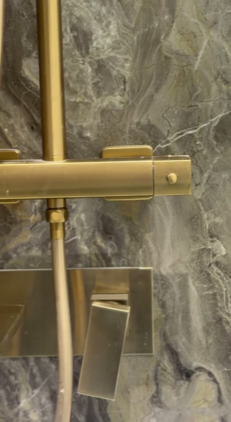 Brushed gold thermostatic shower bar valve and concealed mixer on marble-effect wall