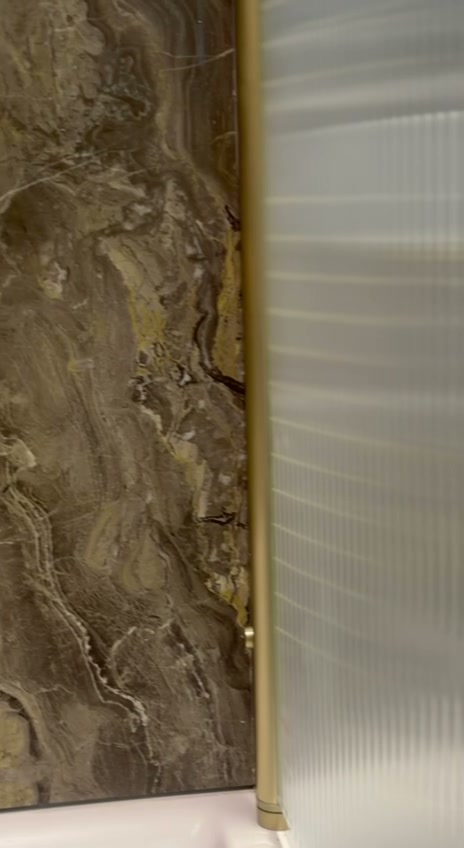 Fluted glass bath screen with brushed gold frame in a luxury bathroom