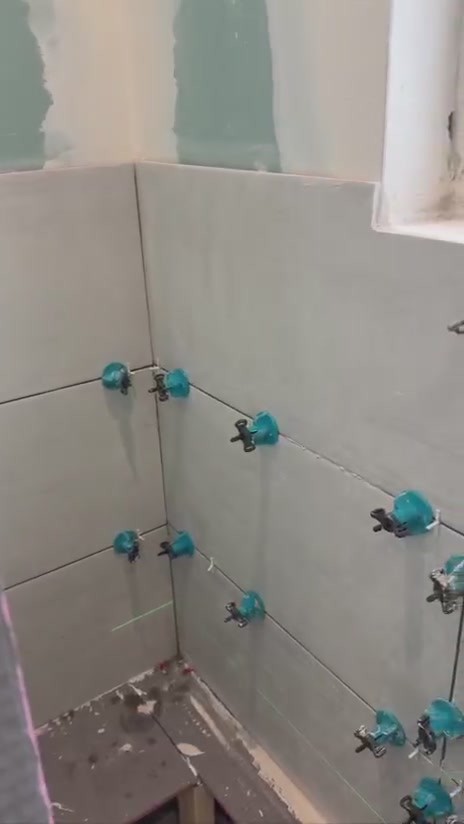 Tile levelling system clips and caps on large format shower wall tiles during a bathroom renovation in Liverpool